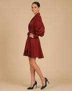 Model in a side pose with a hand on her hip wearing the Elye Mini Wrap Dress in Deep Burgundy Red and black heels.
