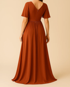 The Terra Maxi Dress with flutter sleeves in burnt orange, made from sustainable recycled polyester chiffon. Shown from the back view. Ethically made in London by ADKN